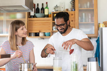 Multi-ethnic couple talking and cooking in kitchen - CUF51654