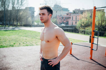 Calisthenics at outdoor gym, bare chested young man taking a break - CUF51684