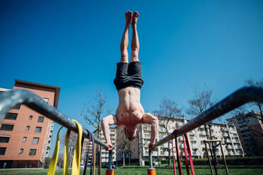 Gymnastik im Freien, ein junger Mann mit nacktem Oberkörper macht einen Handstand am Barren, tiefer Blickwinkel - CUF51691