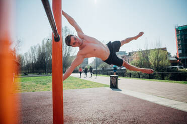 Gymnastik im Freien, ein junger Mann mit nacktem Oberkörper schwingt waagerecht auf einem Trainingsgerät - CUF51693