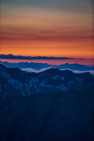 Orangefarbenes Leuchten am Horizont über einer Bergkette, Saas-Fee, Wallis, Schweiz, lizenzfreies Stockfoto