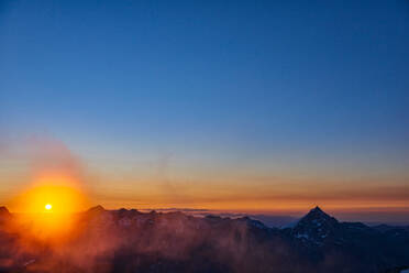 Sun glowing on horizon over mountain range, Saas-Fee, Valais, Switzerland - CUF51756