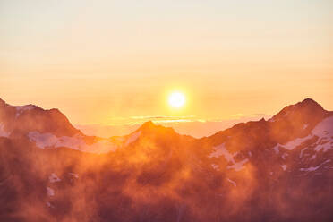 Sun glowing on horizon over mountain range, Saas-Fee, Valais, Switzerland - CUF51758