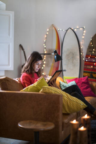 Junge Frau auf dem Wohnzimmersofa mit digitalem Tablet-Touchscreen, lizenzfreies Stockfoto