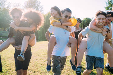 Group of friends piggyback racing in park - CUF51865