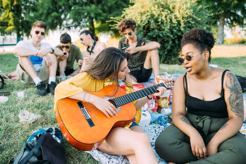 Eine Gruppe von Freunden entspannt sich beim Picknick im Park und spielt Gitarre, lizenzfreies Stockfoto