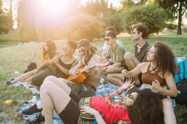 Eine Gruppe von Freunden entspannt sich beim Picknick im Park und spielt Gitarre - CUF51902