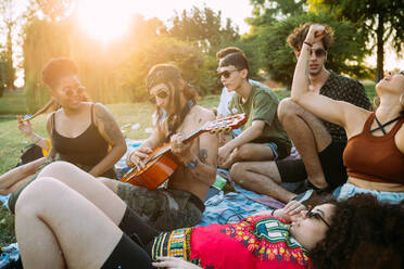 Eine Gruppe von Freunden entspannt sich beim Picknick im Park und spielt Gitarre - CUF51909