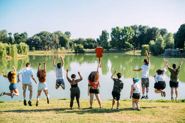Gruppe von Freunden springt vor einem See im Park - CUF51921