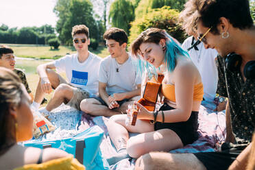 Eine Gruppe von Freunden entspannt sich beim Picknick im Park und spielt Gitarre - CUF51926