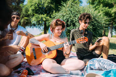 Eine Gruppe von Freunden entspannt sich beim Picknick im Park und spielt Gitarre - CUF51933