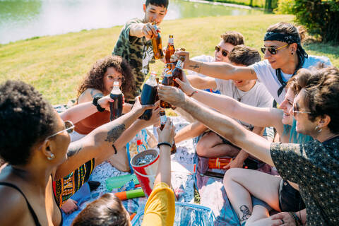 Gruppe von Freunden, die sich bei einem Picknick im Park entspannen und mit alkoholfreien Getränken anstoßen, lizenzfreies Stockfoto
