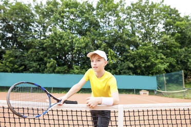 Junge auf dem Tennisplatz, am Netz stehend - KMKF00988