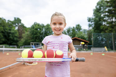 Kleines Mädchen, das Tennis spielen lernt, balanciert Bälle auf einem Schläger - KMKF00990