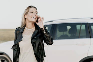 Blond woman using smartphone, white car in the background - ERRF01519