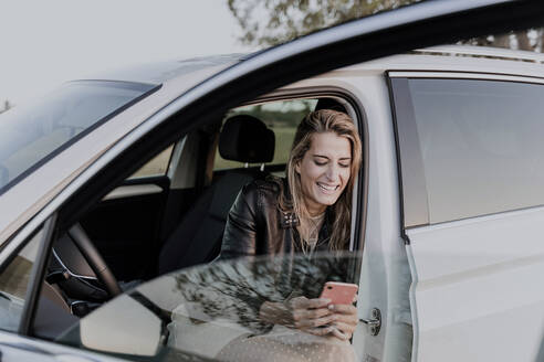 Blonde Frau benutzt Smartphone, sitzt in weißem Auto - ERRF01527