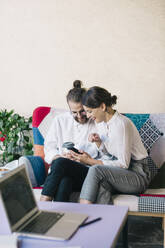 Young couple sitting on a sofa using a smartphone - ALBF00905