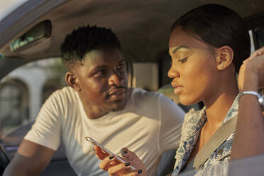 Young couple sitting car, woman using smartphone - VEGF00360