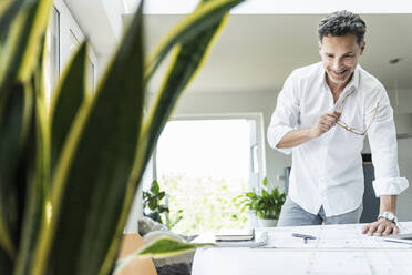 Architect working on blueprint in a bright office, using laptop - UUF18048