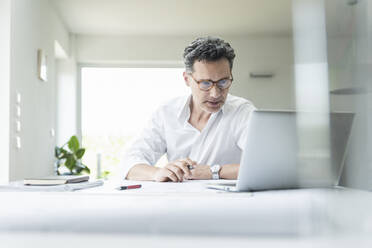 Architect sitting in bright office, using laptop - UUF18052