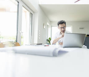 Architect sitting in bright office, using laptop - UUF18053