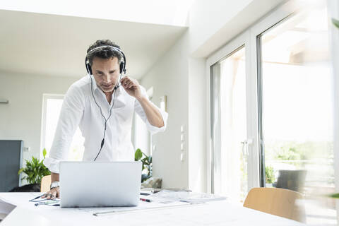 Geschäftsmann in einem hellen Büro, der eine Telefonkonferenz führt, mit Headset und Laptop, lizenzfreies Stockfoto