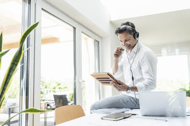 Geschäftsmann in einem hellen Büro, der eine Telefonkonferenz führt, mit Headset und digitalem Tablet - UUF18058