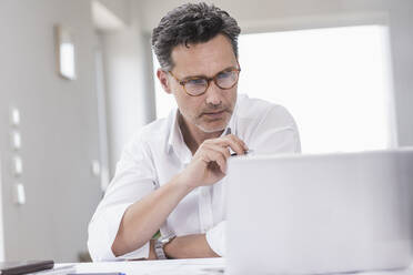 Businessman working in bright office, using laptop - UUF18061