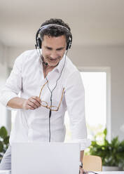 Geschäftsmann in einem hellen Büro, der eine Telefonkonferenz führt, mit Headset und Laptop - UUF18067