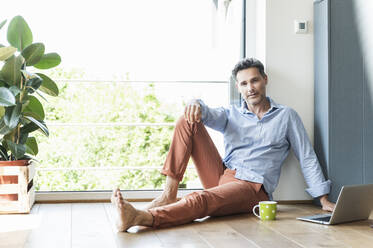 Mature man relaxing at home with a cup of coffee, using laptop - UUF18111
