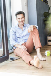 Mature man relaxing at home with a cup of coffee, using laptop - UUF18114