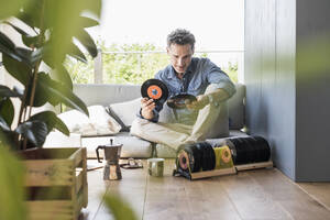 Älterer Mann sitzt zu Hause und schaut sich alte Sigle-Schallplatten an - UUF18119