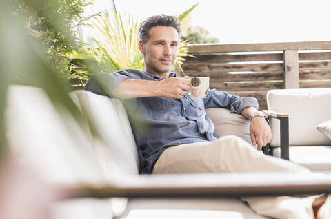 Selbstbewusster Mann, der sich auf der Terrasse entspannt und Kaffee trinkt, lizenzfreies Stockfoto