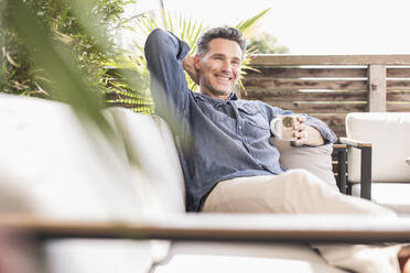 Selbstbewusster Mann, der sich auf der Terrasse entspannt und Kaffee trinkt - UUF18128