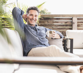 Selbstbewusster Mann, der sich auf der Terrasse entspannt und Kaffee trinkt - UUF18129