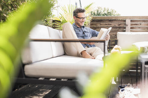 Confident man relaxing on the terrace, reading book - UUF18130