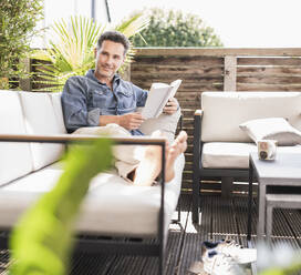 Selbstbewusster Mann, der sich auf der Terrasse entspannt und ein Buch liest - UUF18131