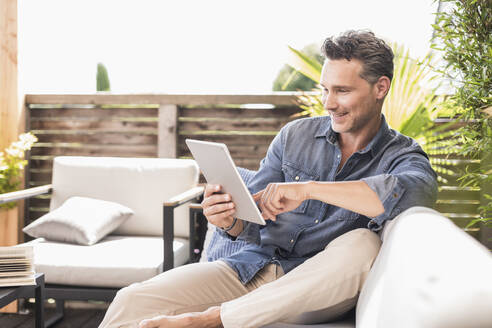 Mature man sitting on terrace, using digital tablet - UUF18138