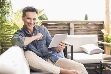 Mature man sitting on terrace, using digital tablet - UUF18139