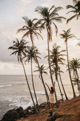 Frau in voller Länge, die sich an Palmen erfreut, während sie das Meer gegen den Himmel in Sri Lanka betrachtet - LHPF00721