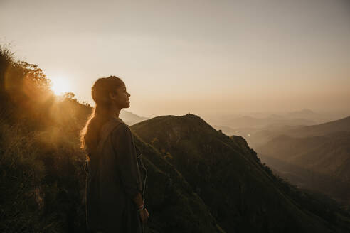 Lächelnder junger Wanderer bei der Erkundung eines Berges gegen den Himmel bei Sonnenuntergang, Sri Lanka - LHPF00729