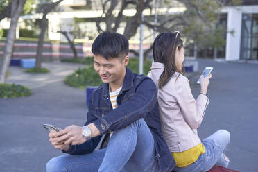 Relaxed couple sitting back to back using cell phones, Barcelona, Spain - DVGF00023