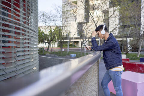 Junger Mann mit Kopfhörern, der auf sein Handy schaut, Barcelona, Spanien, lizenzfreies Stockfoto