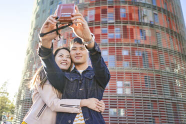 Porträt eines Paares, das ein Selfie mit einer Sofortbildkamera macht, Barcelona, Spanien - DVGF00046