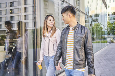 Couple wearing leather jackets walking hand in hand in the city - DVGF00051