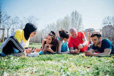 Calisthenics class at outdoor gym, women and men lying on grass looking at smartphones - CUF51955