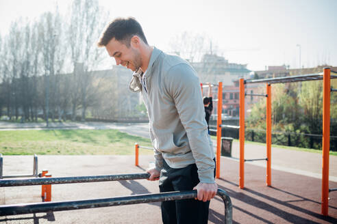 Calisthenics at outdoor gym, young man on parallel bars - CUF51959