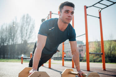 Gymnastik im Freien, junger Mann macht Liegestütze an einem Trainingsgerät - CUF51968