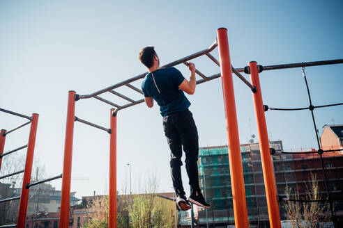 Gymnastik im Freien, junger Mann macht Klimmzüge an einem Trainingsgerät, Rückansicht - CUF51969