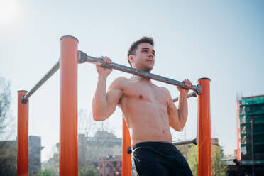 Gymnastik im Freien, ein junger Mann mit nacktem Oberkörper macht Klimmzüge an einem Trainingsgerät - CUF51972